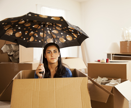 A girl sits inside a moving box holding an umbrella