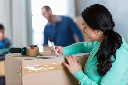 Woman preparing list and packing boxes for move.