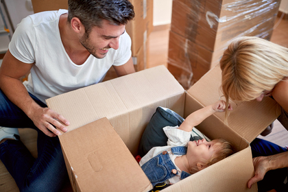 Parents playing with their daughter hiding in cardboard box.